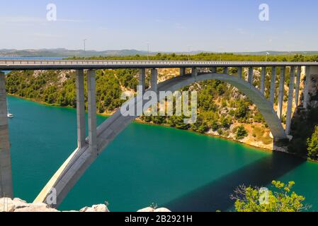 Stahlbetonauto lange hohe Bogenbrücke über den Fluss Krka in Kroatien bei Sibenik. Malerische kroatische Flusslandschaft im Frühling Stockfoto