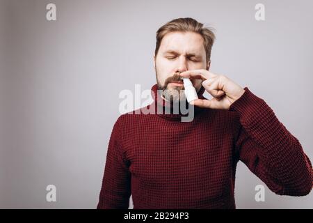 Porträt des bärtigen Mannes im warmen Strickpullover im Studio mit geschlossenen Augen und nasalem Spray. Reife Kranke sprühen medizinische Präpara Stockfoto