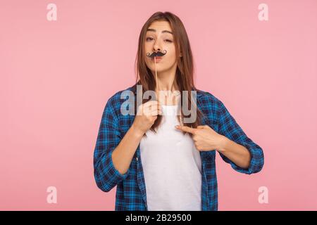 Porträt eines verspielten Mädchens in kariertem Hemd, das falschen geschweiften Schnurrbart auf dem Stock hält und sich zeigt, wobei es Spaß macht, sich als bossy und arrogant zu behaupten. Stockfoto