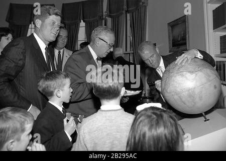 Als er die Route seines Orbitalflugs zeichnete, signiert Astronaut Oberstleutnant John H. Glenn, Jr. (rechts) bei einem Empfang zu seinen Ehren den "Fliers' and Explorers' Globe" der American Geographical Society (AGS) im Oval Office of the White House. Präsident John F. Kennedy (ganz links), Vizepräsident Lyndon B. Johnson (hinten), AGS-Direktor Charles B. Hitchcock (im Profil, mit Brille) und mehrere Kinder, darunter Präsident Kennedys Neffe Robert F. Kennedy, Jr. (im Vordergrund, zweite von links), sehen von links. Stockfoto