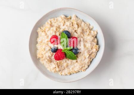Haferbrei Porridge in einer Schüssel mit frischen Beeren und Minze auf weißem Hintergrund für gesundes Diät-Frühstück. Draufsicht Stockfoto