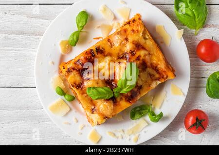 Fleischlasagna mit frischem Basilikum und Parmesankäse auf einem Teller auf weißem Holztisch. Draufsicht. Italienische Küche. Stockfoto