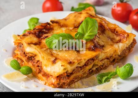 Hausgemachtes Fleisch Lasagne mit frischem Basilikum und Parmesankäse auf einem Teller auf weißem Holztisch. Nahaufnahme. Italienische Küche. Stockfoto