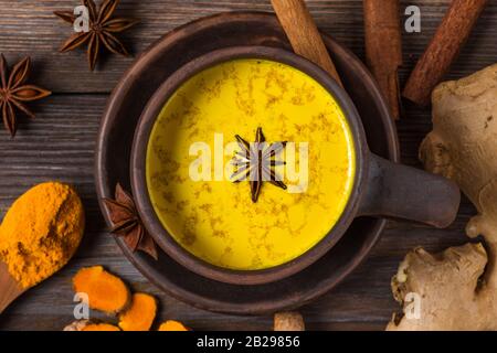 Becher aus goldener Milch oder turmiger Latte mit Curcuma, Sternanis, Ingwer und Zimt auf rustikalem Holztisch. Draufsicht. Gesundes Getränk. Stockfoto