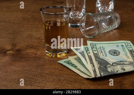 Schuss Whisky und leere Schussgläser auf Holz mit amerikanischem Geld Stockfoto