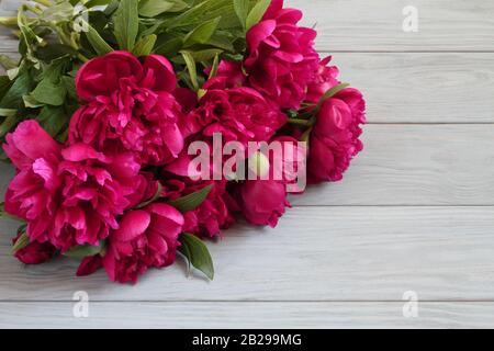 Blumenstrauß aus dunkel rosa Pfingstrosen liegen auf grau Holztisch Stockfoto