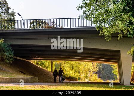 Silhouettenansicht des Wanderpaares leit im Park am Wannsee in der Herbstsaison einen Hund unter die Brücke. Stockfoto