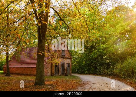 Ruhige Landschaft mit kleinem, groben alten Ziegelhaus, Park und Straße in ländlicher Umgebung im Herbst ohne Menschen und Sonneneinfallslicht. Stockfoto