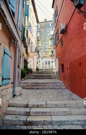 Senkrechtes Bild der Treppe in der mediterranen Gasse der Stadt Rovinj mit rotem Gebäude auf der rechten Seite und orange auf der linken Seite Stockfoto