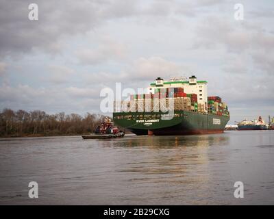 Savannah, GA - 23. FEBRUAR 2020: Ein Schleppboot hilft, von hinter einem großen Frachtschiff zu führen, das mit Transportbehältern aus dem Hafen von Savannah o geladen ist Stockfoto