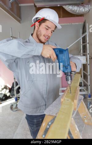 Zimmermann bohrt ein Loch mit einem elektrischen Bohrer auf Holz Stockfoto