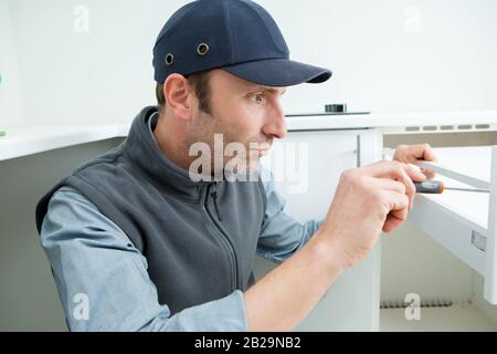 Handwerker in Latzhosen Reparatur Schrank in der Küche Scharnier Stockfoto