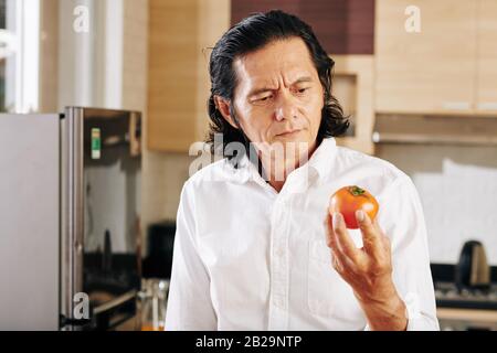 Porträt des frostigen, reifen Mannes, der frische reife Tomaten in der Hand betrachtet Stockfoto