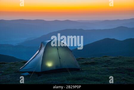 Beleuchtetes Zelt gegen Sonnenaufgangsszene in den Bergen. Stockfoto