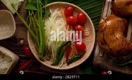 Draufsicht auf Zutaten Somtum oder Papaya-Salat, thailändische traditionelle Küche mit auf Holztablett gegrilltem Huhn Stockfoto