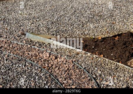 Metalleinkantung, die Schmutz und verschiedene Schotterfarben in einem Park voneinander trennt Stockfoto