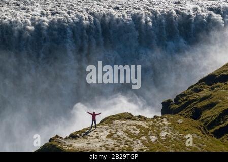 Berühmter Island-Riese-Wasserfall und Frau in Rot gekleidet für die Proportionalität im Vordergrund. Stockfoto