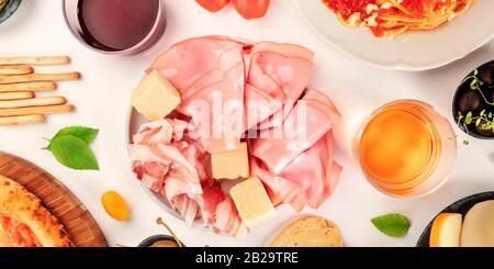 Italienische Charcuterie, flaches Laienpanorama. Eine Auswahl an Schinken und Käse, von oben auf weißem Hintergrund mit Weingläsern aufgenommen Stockfoto