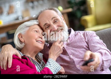 Grauhaarige lächelnde Frau, die ihren Ehemännchenbart berührt und nachdenklich aussieht Stockfoto