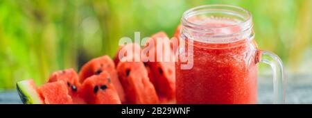 Glas Wassermelonen-Smoothie und ein Stück Wassermelone auf einem HOLZTISCHBANNER, LANGFORMAT Stockfoto