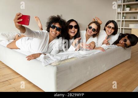 Fröhliche diverse Mädchen, die Sonnenbrille tragen, die selfie auf der Party mitnimmt Stockfoto