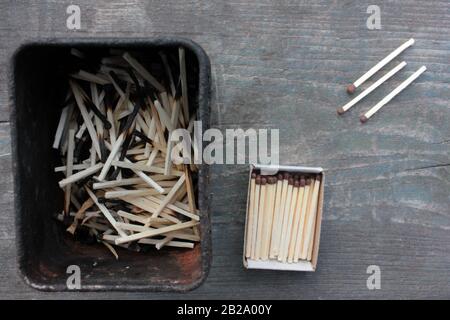 Streichholzschachtel mit nicht verwendeten Streichhölzern und verbrannten Streichhölzern in alter Zinnschachtel auf einem rauen Holztisch. Dunkle Farben. Draufsicht. Kopierbereich Stockfoto