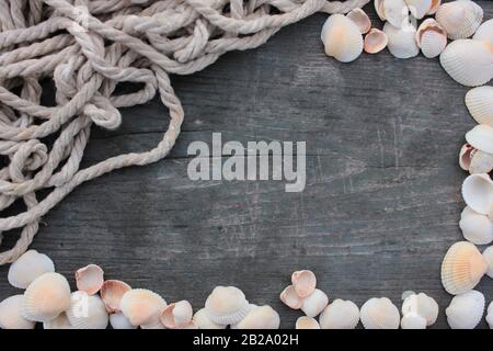 Sommer-Rahmen mit Schalen und Seil auf einem grob rissigen dunklen Holzhintergrund Stockfoto