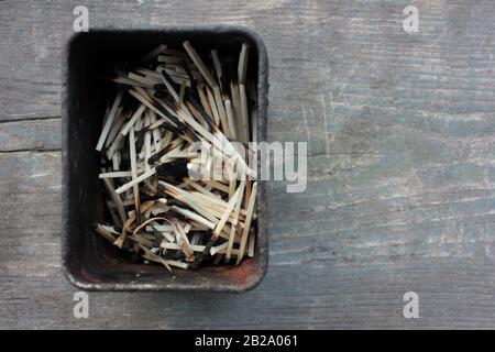 Verbrannte Streichhölzer in alter Blechdose auf einem rauen Holztisch. Dunkle Farben. Draufsicht. Kopierbereich Stockfoto