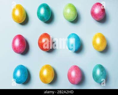 Osterfestliche Knollenzusammensetzung aus bunt bunt bemalten, glänzenden Ostereiern, die auf hellblauem Pastellhintergrund aufliegen. Draufsicht, flacher Lay. Stockfoto