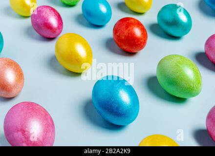 Ostern kreative Festlichkeit aus bunt bunt bemalten, glänzenden Ostereiern, die in diagonalen Linien auf hellblauem Pastellhintergrund ausgelegt sind. Se Stockfoto