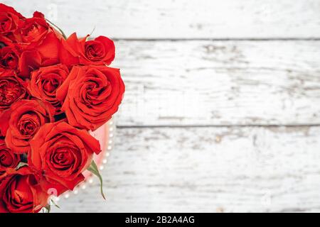 Ein Blumenstrauß aus scharlachroten Rosen für das Valentinstags-Verzierungen-Konzept mit weißem Holzhintergrund. Liebe und Romantik Stockfoto