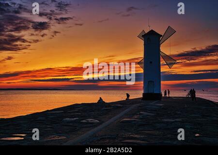 Sonnenuntergang mit Touristen am windmühlenförmigen Leuchtturm an der Ostsee in Swinemünde. Swinoujscie, Polen Stockfoto