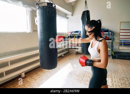 Boxerin schlägt einen riesigen Stanzbeutel im Fitness-Fitnessstudio. Frau übt ihre Schanzen in einem Boxstudio Stockfoto