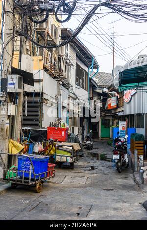 Unordentliche und unsaubere Gassen mit Mülltonnen und elektrischen Kabeln, die an einem Strompfosten in Thailand hängen Stockfoto