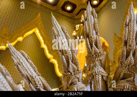 Aus Keramik geschnitzte mehrköpfige Schlange vor einer goldenen Statue des Buddha mit einer Safrangarbe im verzierten Wat Songkhram, Bangkok, Thailand Stockfoto