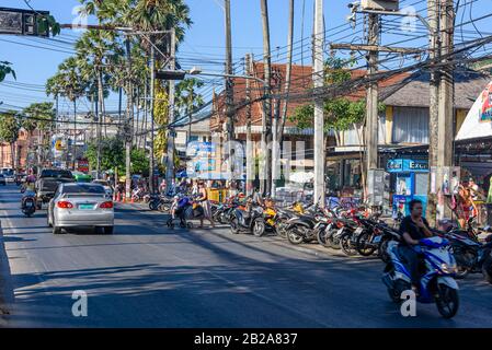 Eine Reihe von Rollern parkte an der Seite einer Straße und Verkehr auf der Straße am Kata Beach, Thailand. Stockfoto