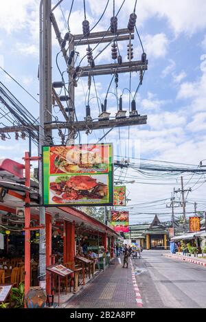 Unordentliche und unsaubere elektrische Kabel hängen an einem Strompfosten an einer Straße vor Restaurants, Thailand Stockfoto