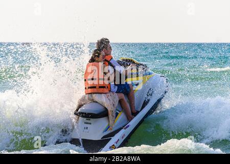 Mann und Frau chinesische Touristen auf einem gemieteten Jetski, der in den Wellen spritzt, Patong Beach, Phuket, Thailand Stockfoto