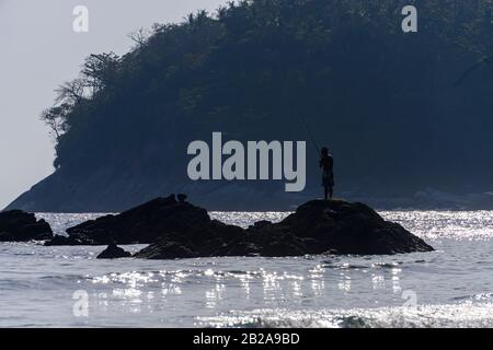 Ein Mann fischt aus Felsen mit Angelrute, Kata Beach, Phuket, Thailand Stockfoto