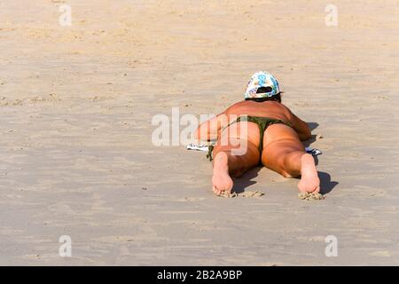 Eine übergewichtige Frau liegt beim Sonnenbaden am Strand auf dem Bauch Stockfoto