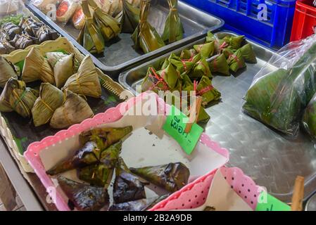 Klebrige Reiskugeln, die mit Bananenblättern umhüllt sind, die in einem thailändischen Marktstall in Thailand zum Verkauf angeboten werden Stockfoto