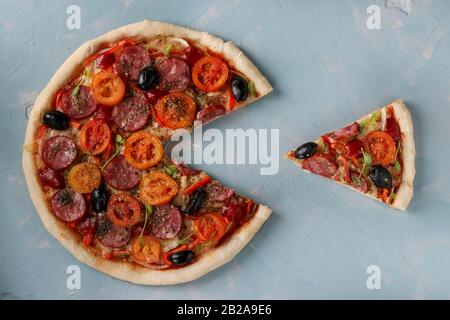 Pizza mit einem ausgeschnittenen Stück auf hellblauem Hintergrund, Closeup Stockfoto