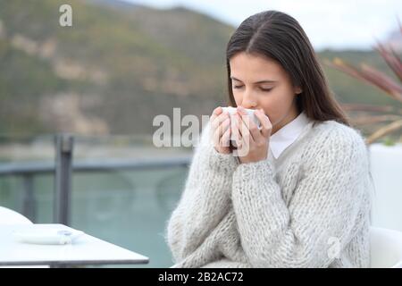 Das Mädchen riecht ihren Kaffee, der in einer Café-Terrasse in einem See in den Bergen sitzt Stockfoto
