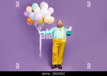 Lange Foto von positiv aufgeregt funky Mann mit großem Bauch halten viele Luftkugeln Baloons ziehen rosa Hosenträger tragen helle Teelhosen Schuhe Stockfoto