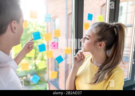 Geschäftsleute treffen sich im Büro und verwenden Post-it-Notizen, um Ideen auszutauschen. Brainstorming-Konzept. Haftnotiz an der Glaswand. Stockfoto