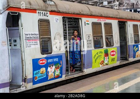 Mumbai, Indien - 29. Februar 2020: Junge Indianerin steht mit einem Telefon am Chatrapati Shivaji Terminus in der Eisenbahn-Triebwagentür Stockfoto