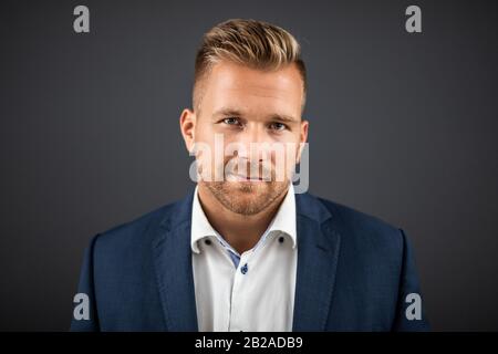 Gutaussehender Mann, der über dunkelgrauem Hintergrund steht und auf die Kamera blickt. Portrait man Konzept. Stockfoto
