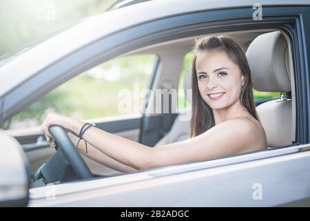 Schöne junge Frau, die mit einem Lächeln im Innenraum eines neuen Autos sitzt. Er ist froh, dass er ein Fahrer ist. Stockfoto