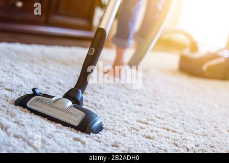 Junge Frau mit Staubsauger beim Reinigen des Teppichs im Haus. Stockfoto