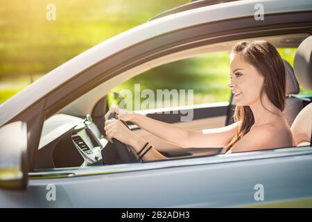 Schöne junge Frau, die mit einem Lächeln im Innenraum eines neuen Autos sitzt. Er ist froh, dass er ein Fahrer ist. Stockfoto